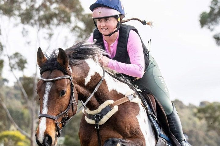 smiling rider jumping her horse in pink base layer and sage riding tights