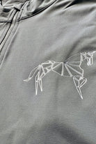 Close-up of a gray V1 Motion Short Sleeve - Grey featuring a geometric white horse design printed on the chest. The image highlights the intricate lines and angles forming the abstract horse figure, perfect for rider wear. The fabric of the V1 Motion Short Sleeve - Grey from Pure Canter appears smooth and slightly textured, providing moisture wicking comfort.