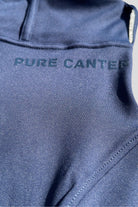 Close-up of navy blue V2 Fusion Riding Tights - Navy with the text "PURE CANTER" printed in dark blue on the smooth, synthetic fabric. The material appears tailored for athletic wear, perfect for equestrian fashion and Pony Club suitable activities.