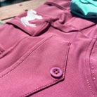 Close-up view of vibrant pink **V1 Fusion Riding Tights - Mulberry** with a button, pocket detail, and a white logo of a horse on the performance fabric by **Pure Canter**. A light blue object is slightly visible in the background.