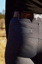 Close-up of a person from the waist down wearing form-fitting dark gray Pure Canter V2 Fusion Riding Tights - Dark Grey with small dots on the seat and upper thigh areas for grip, embodying equestrian fashion. They are also wearing a brown belt threaded through the belt loops and a black waistband from a shirt or jacket.