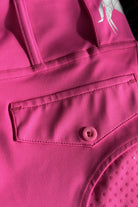 Close-up of vibrant pink V2 Fusion Riding Tights - Hot Pink by Pure Canter featuring a front flap pocket with a button. The smooth performance fabric shows visible stitching along the pocket edges. On the upper part of this equestrian fashion garment, there is a small reflective design.