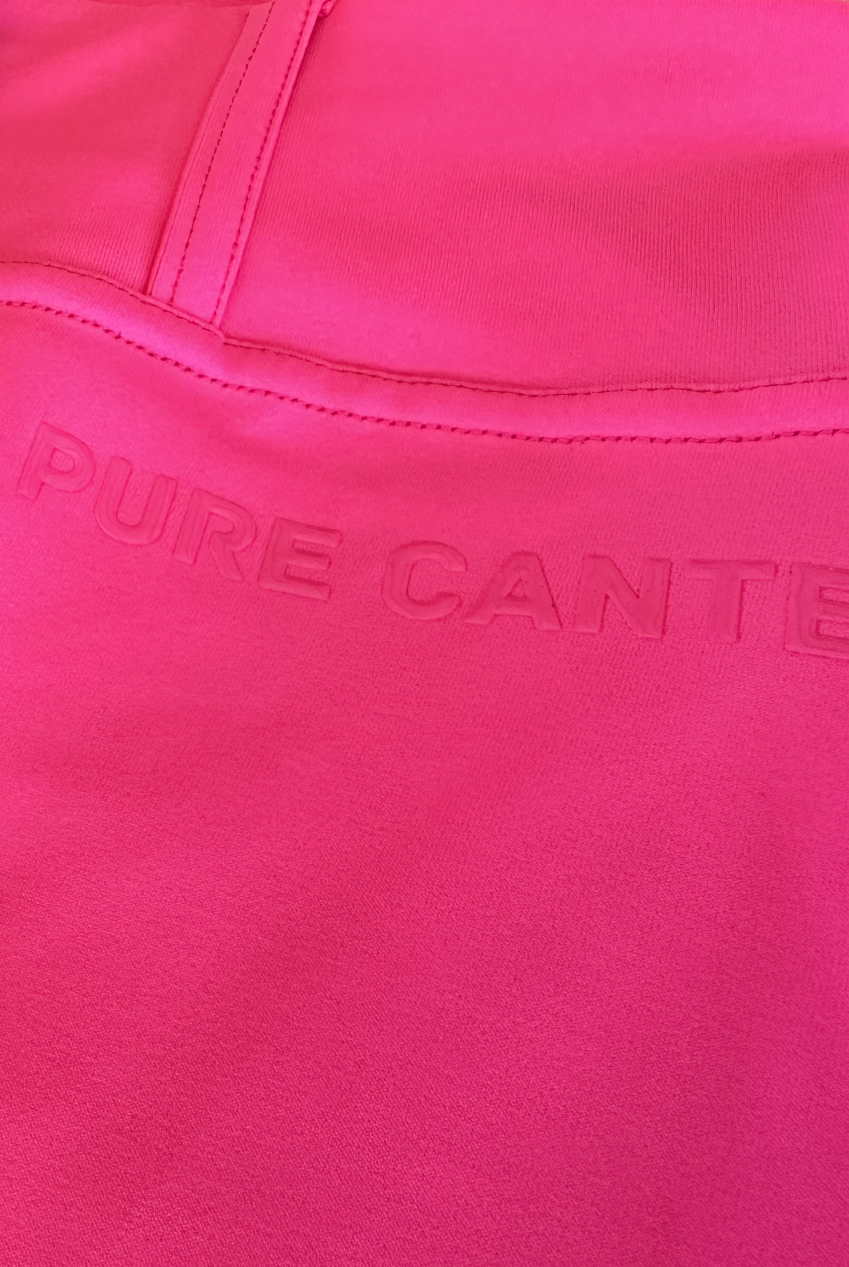 A close-up image of a bright pink garment with the embossed text "PURE CANTE" on the fabric. The stitching is visible along the seam, indicating a section of clothing, possibly a pocket or waistband area, typical in equestrian fashion. The product shown is Fusion Tights G2 - Hot Pink by Pure Canter.
