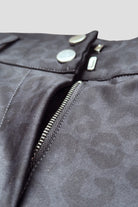 Close-up of an unzipped pair of The Breeches - Black Leopard by Pure Canter featuring a grey animal print pattern. The image prominently displays the open zipper and two metallic buttons above it. Made from performance fabric, the breeches have a smooth texture and are designed with a Silicone Seat for added grip.