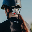 Person wearing a black helmet and a black shirt with "PUR" printed on it. Their long hair is tied back with one of those beautiful **Pure Canter Pty Ltd Oversized Scrunchies**, and they are facing away from the camera against a blurred, outdoor background.