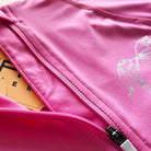 A close-up image of a partially unzipped pink jacket, revealing an orange inner lining. The Motion Top Long - Pink by Pure Canter, designed for quick drying and moisture wicking, features a geometric pattern on the right side. The zipper is white with a black zip pull.